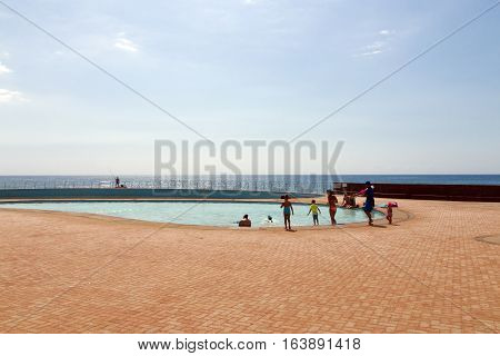 People Swimming In Seaside  Pool Against Ocean Skyline