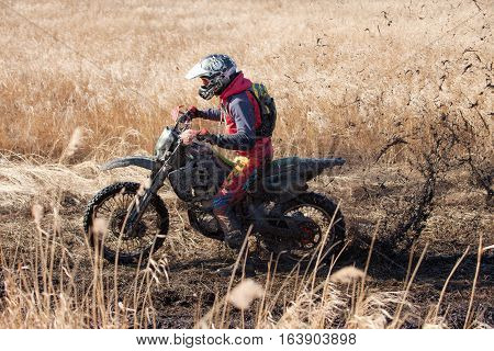 KHABAROVSK RUSSIA - OCTOBER 23 2016: Enduro bike rider on a field with dry grass in autumn. The motorcycle skids and makes a lot of mud splashes