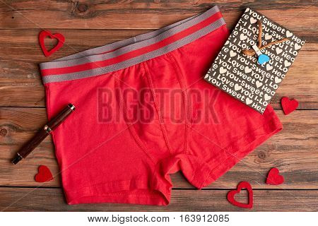 Boxer briefs on wooden background. Fabric hearts near paper bag. Romantic gift for men.