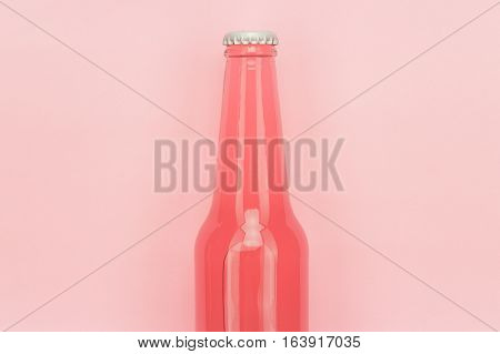 glass bottle of pinkish soda drink on pink background