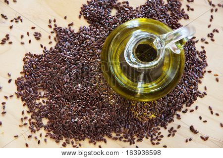 Brown flax seeds and linseed oil in a glass jug on a wooden kitchen board top view from above