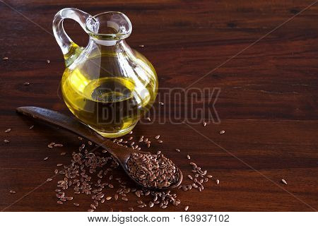 flax seeds on a spoon and linseed oil in a glass jug on a dark wooden table copy space