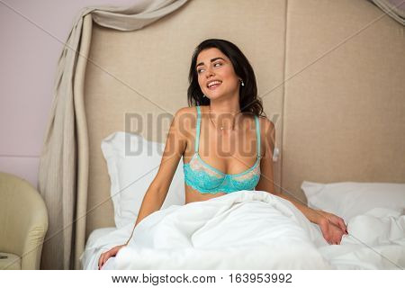 Woman sitting on bed. Young female in bra. Awake after long sleep.