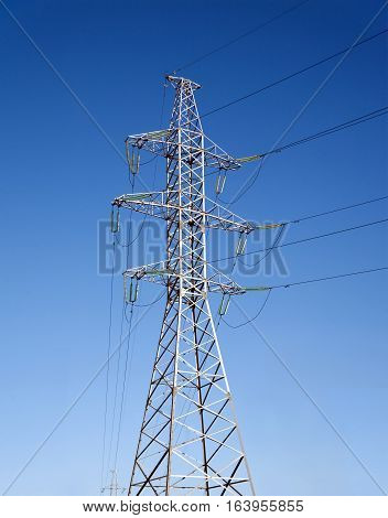 High-voltage power line grey metal prop with many wires vertical view over clear cloudless blue sky vertical view