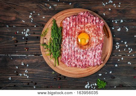 Homemade raw minced meat with egg and herbs closeup top view.