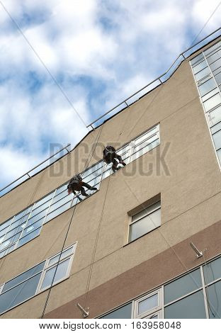 Two industrial climbers with cleaning equipment, washes windows in a hign office building