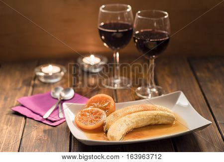 Bananes flambe with caramelized oranges with two glasses of wine in rustic style