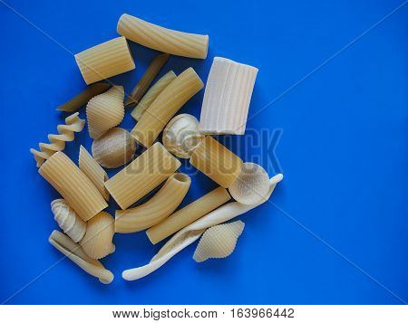 Many different types of Italian pasta including penne macaroni (maccheroni) fusilli spaghetti trenette (linguine) orecchiette tortiglioni conchiglie (shells) - blue background with copy space