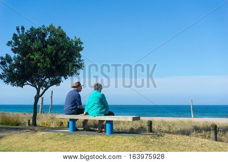 Mount Maunganui, December 21, 2016; Eldery couple rest and look at scenic ocean view on becnh seat along Mount Maunganui ocean-beach