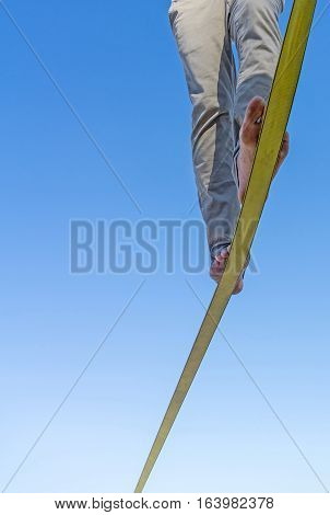 Two feet and legs on slack-line tape high in air against blue sky with balance and detrmination reaching the end slack-line