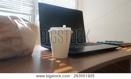 A Businessmans Desk With A Disposable Cup For Coffee And Fast Food. Open Laptop Computer. Breakfast 