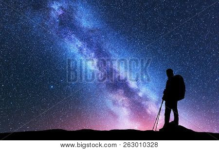 Silhouette Of Man With Backpack And Trekking Poles Against Amazing Purple Milky Way At Night. Space.