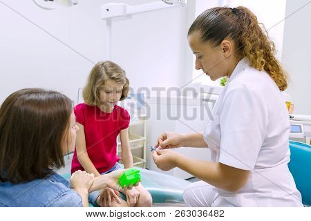 Mother And Little Daughter Visiting Dentist At Dental Clinics. Orthodontist Puts On, Corrects The De