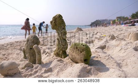 Sand Castle On The Beach, Coral Ejected By The Sea To Shore, An Unrecognizable Family Walks On A Pub