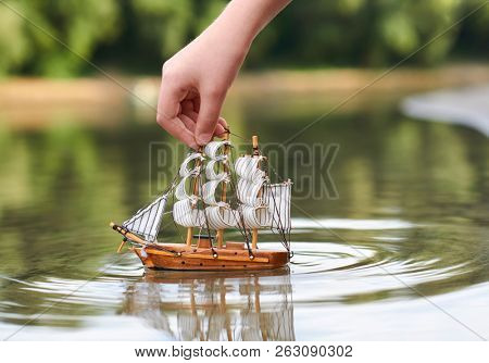 girl playing with a toy sailing ship by the river, hand closeup