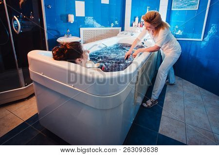 Young Woman During Hydromassage In Beauty Salon. Concept Of Body Care And Spa. The Masseuse Massages