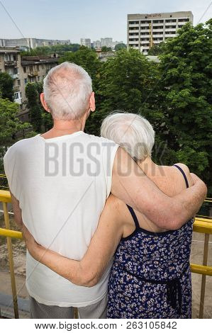Senior Couple Standing Oustide At Balccony At Home And Looking Awayat Green Trees