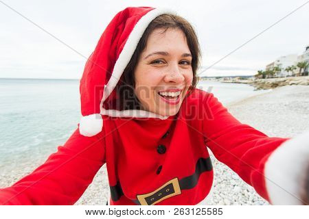 Christmas, Humor And People Concept - Young Woman In Santa Suit Making Selfie Near The Sea At Summer