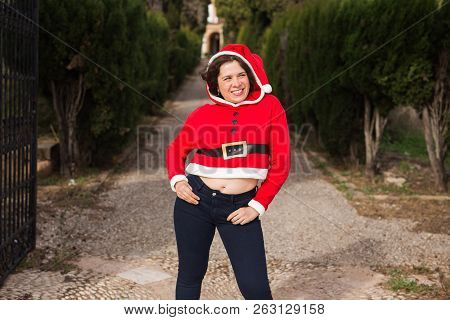 Christmas, Holidays, Humor And People Concept - Young Happy Woman In Santa Suit Dancing Outdoors