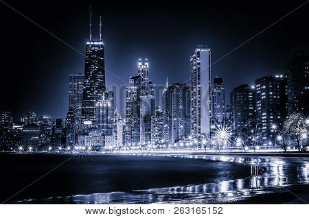 Glowing Chicago Skyline at Night. Iconic view of the Windy City's vibrant downtown from Lakefront Trail at North Avenue Beach along the Gold Coast. Blue stylized cityscape with copy space.