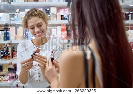 Positive Female Consultant Showing New Lipsticks And Helping With Choice In Cosmetics Store. Long Ha