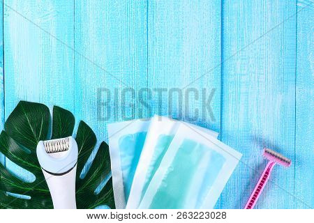Means For Hair Removal. Epilator, Razor For Shaving, Wax Strips On A Tropical Leaf On A Blue Wooden 