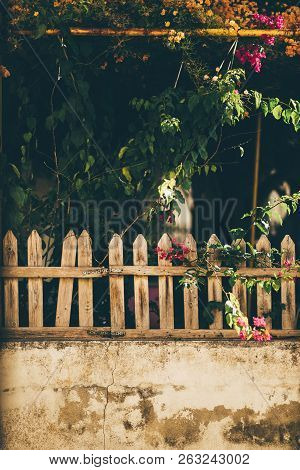 Vertical Shot Of A Small Wooden Fencing With An Old Concrete Wall Behind With Cracked Plaster On It,