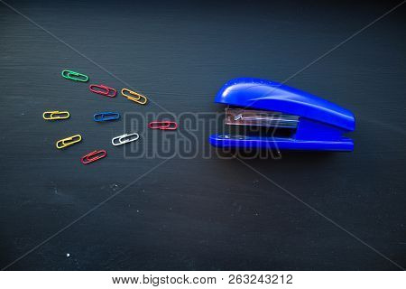 A Stepler And Colored Clips On Black Background