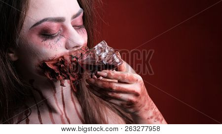 A Girl With A Horrible Halloween-style Make-up Drinks Red Liquid From A Skull-shaped Glass. Horror S