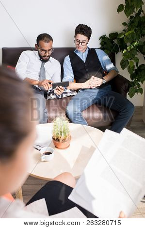 Erious Concentrated Young Multi-ethnic Men Sitting On Sofa And Testing New Mobile App On Smartphone 