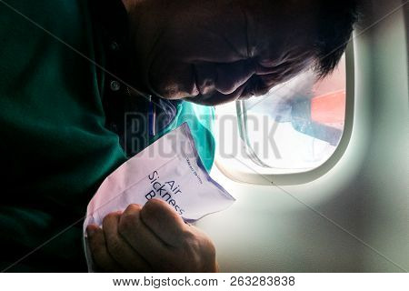 Suffering Asian Man Holding Air Sickness Vomit Bag In Airplane