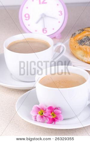 两杯咖啡与时钟和面包在背景中。