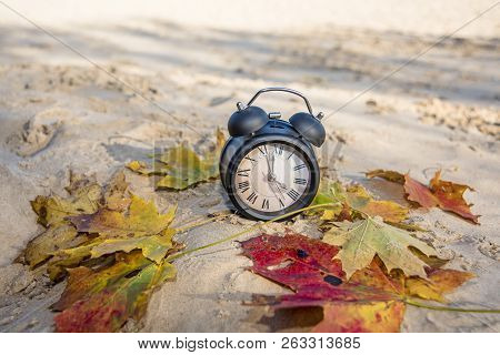 Vintage Black Alarm Clock On Autumn Leaves. Time Change Abstract Photo.