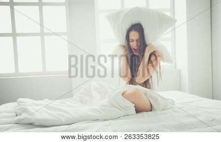 Young caucasian woman covering her head and ears with pillows.