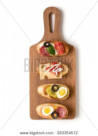 Open faced sandwich canape or crostini on a wooden serving board isolated on white background closeup. Top view.