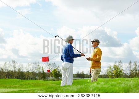 Two active friendly men with golf clubs discussing the forthcoming game on new play area