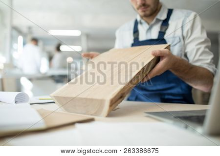 Contemporary professional cabinetmaker holding piece of wood over desk