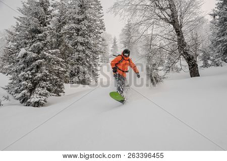 Man Riding Down The Hill On The Green Snowboard On The Powdered Snow In The Mountain Tourist Resort 