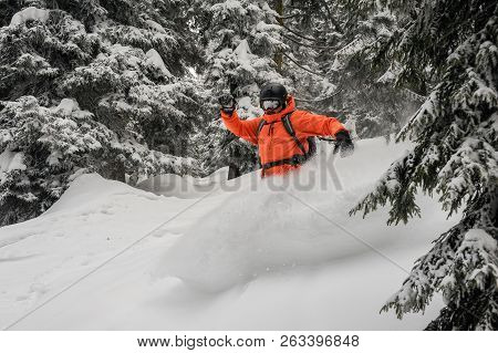 Man Riding Down The Hill On The Green Snowboard Between The Trees Making Snow Splash In The Mountain