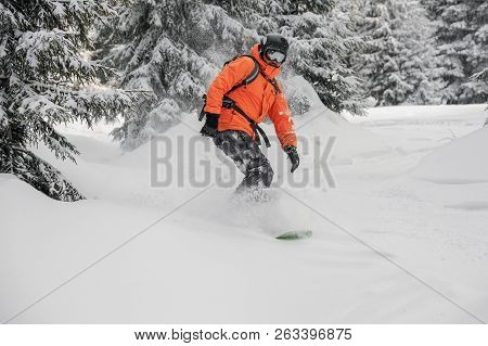 Man Riding Down The Hill On The Green Snowboard Between The Snowcovered Trees In The Mountain Touris