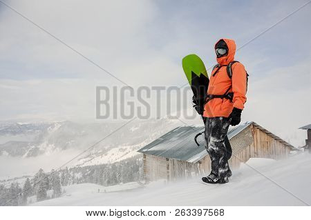 Man Standing With The Snowboard In Hands Onthe Hill In The Mountain In The Popular Tourist Resort In