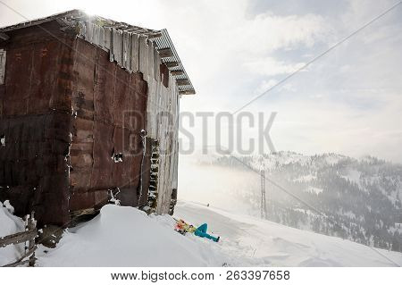 Girl Lying On The Snowboard Near The Building In The Mountain And Looking Into A Distance In The Pop