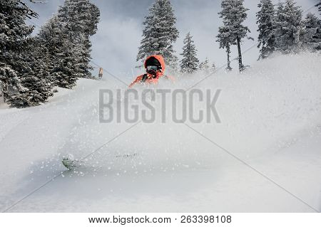 Man Running Down The Mountain Hill On The Snowboard Making Splash On The Background Of Trees And Sky
