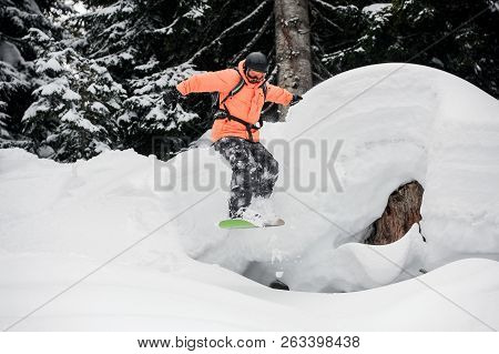 Man Jumping From The Mountain Hill On The Snowboard On The Background Of Trees In The Mountain Touri