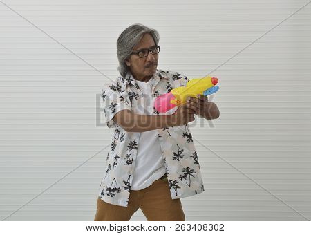 Senior Traveler Asian Man Wearing Glasses, Summer Shirt And Brown Shorts Holding Colorful Water Gun 