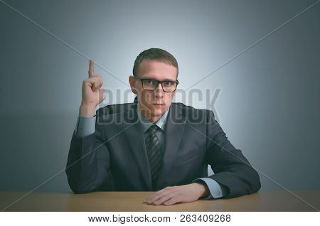 Serious Businessman Is Showing Up By His Index Finger By Sitting By The Table And Have A New Busines
