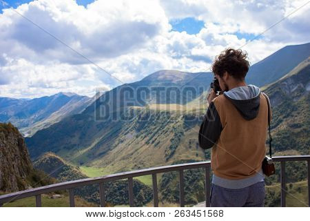 Young Curly Traveler Taking Photo With Camera In Kazbegi. Beautiful View Of Kazbegi In Autumn