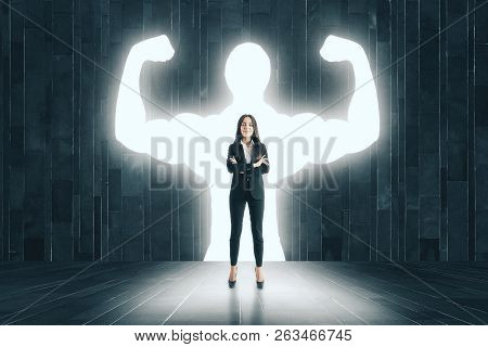 Businesswoman With Muscly Arms In Concrete Interior. Confidence And Power Concept
