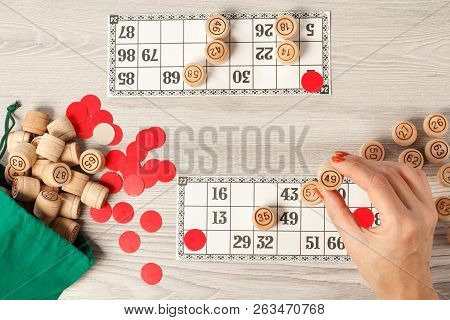 Female Hand Holding A Barrel For A Game In Lotto. Wooden Lotto Barrels With Green Bag, Game Cards An