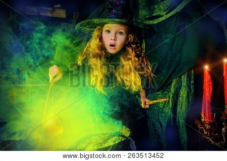 Happy Halloween. Cute child girl in witch costume is in a witch's lair. Cute cheerful little witch cooks a magic potion. 